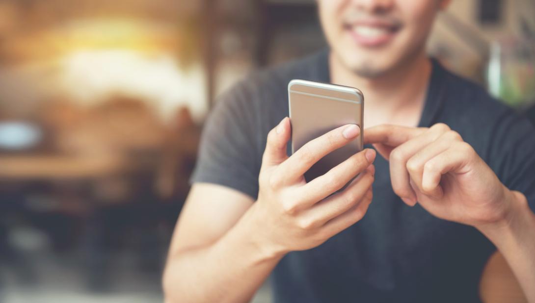 Smiling man holding a smartphone in front of him.